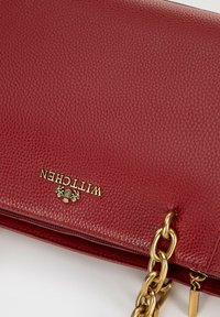 Red leather crossbody bag with a textured surface, gold hardware, and a chunky chain strap. Features embossed brand name and zipper closure.