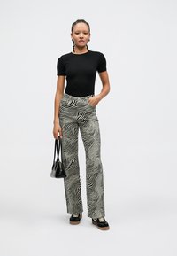 Camiseta negra ajustada, pantalones de talle alto con rayas de cebra en blanco y negro, zapatillas negras y un pequeño bolso negro.