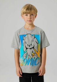 Szara bawełniana koszulka z dużą grafiką Sonic w czerni i niebieskim, z napisem „Sonic” w gradiencie niebieskiego i zielonego. Krótkie rękawy.