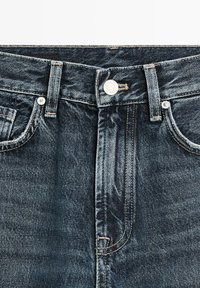 Dunkelblaue Jeans aus Denim mit Knopfverschluss, Gürtelschlaufen und Vordertaschen, die die strukturierte Stoffoberfläche und Nahtdetails zeigen.