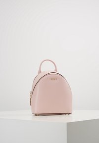Mini růžový batoh vyrobený z texturované kůže, s kulatým tvarem, zlatými kovy a horním madlem. Zipové uzavření na boku.