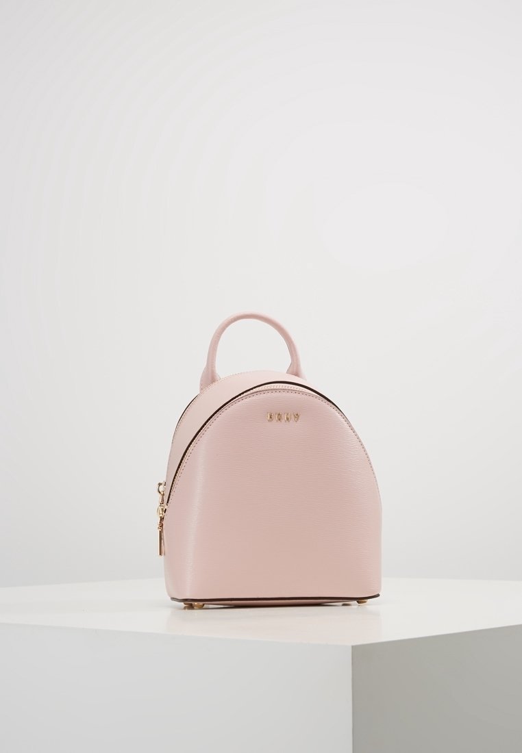 Mini růžový batoh vyrobený z texturované kůže, s kulatým tvarem, zlatými kovy a horním madlem. Zipové uzavření na boku.
