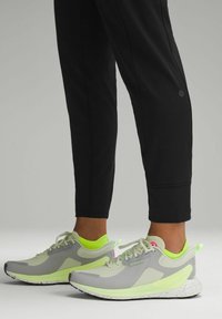 Grå och neongröna sportskor med nät- och texturerad ovandel, snören och en fläckig sula, kombinerade med svarta åtsittande träningbyxor.