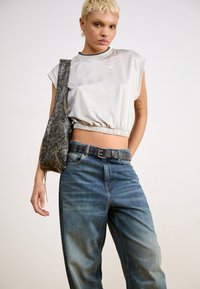 Light grey, cropped, short-sleeve top with elastic hem; blue denim, relaxed-fit jeans; black studded belt; textured dark bag.