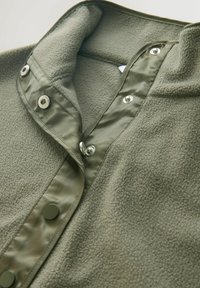 Oliven grøn fleece skjorte med høj krave, der har flade trykknapslukninger og en blød tekstur. Stoffet kombinerer varme med en vandafvisende finish.