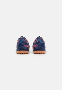 Achteraanzicht van sportschoenen met een marineblauwe bovenkant met roze spetteraccenten en een gestructureerde bruine rubberen buitenzool.