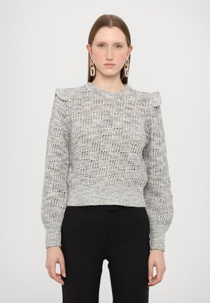 Ljusgrå stickad tröja med texturerat mönster, volangdetalj vid axlarna och ribbad nederkant. Modellen bär svarta byxor.