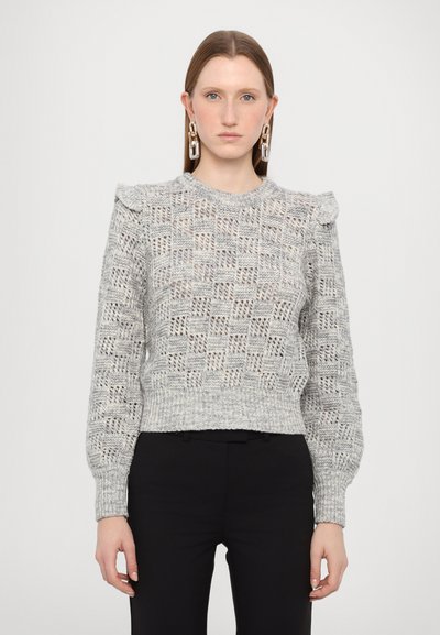 Lysegrå strikket sweater med tekstureret mønster, volangdetalje på skuldrene og ribbet kant. Modellen har sorte bukser på.
