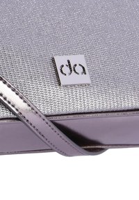 Bolso de mano metálico plateado con superficie texturizada, una correa púrpura brillante y una placa de logo cuadrada ubicada en el frente.