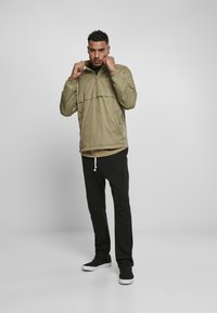 Lys olivengrøn pullover jakke med halvlukning, sidelommer og elastiske manchetter. Parret med sorte sweatpants og slip-on sko.
