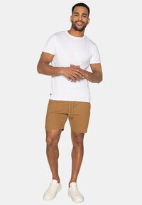 Brune shorts med snøre i taljen, parret med en ensfarvet hvid T-shirt og hvide sneakers. Enkel, afslappet design uden synlige mønstre.