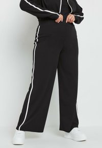 Czarne szerokie spodnie z białymi bocznymi paskami, wykonane z miękkiego materiału. Posiadają wysoki stan i zwężaną nogawkę z delikatnym otwarciem przy kostce.