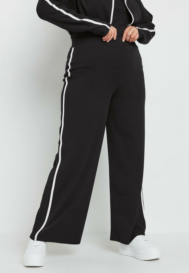 Czarne szerokie spodnie z białymi bocznymi paskami, wykonane z miękkiego materiału. Posiadają wysoki stan i zwężaną nogawkę z delikatnym otwarciem przy kostce.