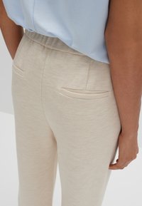 Lichtbeige textuur broek met een gladde afwerking, voorzien van twee achterzakken en een elastische tailleband, gecombineerd met een lichtblauw top.