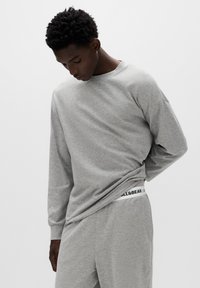 Szara koszula z długim rękawem wykonana z miękkiego materiału, o zaokrąglonym dekolcie, luźnym kroju, zestawiona z szarymi spodniami na gumce z logo.