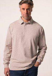 Světle béžová dlouhá polo košile vyrobená z měkké tkaniny, s límečkem, knoflíkovou légou a jemnou strukturou. Nositá s tmavě modrými džínami.