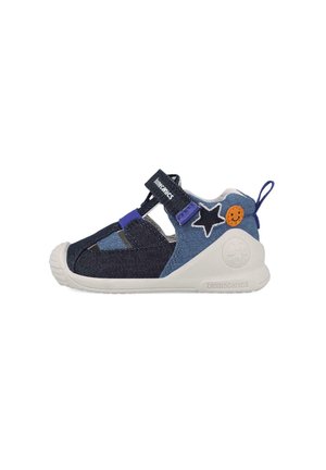 Zapato textil en azul y marino con suela de goma moldeada, correa de Velcro, acentos de estrella y cara sonriente, y diseño lateral cortado para mayor transpirabilidad.