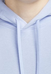 Närbild av en ljusblå huvtröjas halsringning med huva och dragsnören synliga.