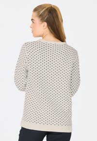 Cremefarbener Pullover mit einem schwarzen Herzmuster, Rundhalsausschnitt und geripptem Saum. Das Design umfasst lange Ärmel und eine lockere Passform.