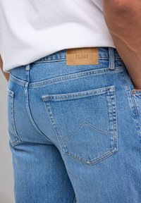 Jeans de mezclilla de color azul claro con cintura alta, que cuentan con una etiqueta de cuero marrón que dice "AMERICA TODAY" y costuras en contraste, además de un bolsillo con un diseño puntiaguado.