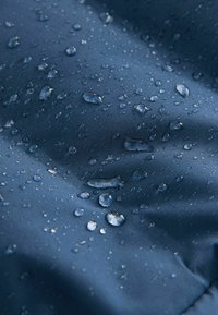 Gouttes d’eau de différentes tailles sur une surface en tissu lisse bleu foncé, suggérant une résistance à l’eau ou un matériau étanche.