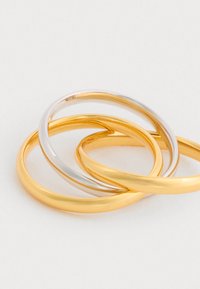 Kolm õhukest metallringi, mis on omavahel p�õimunud; kaks neist on kuldse tooni ja üks hõbedase tooni, siledat, läikivat pinnaga ja ümarat kuju.