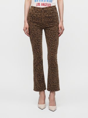 Femme portant un pantalon slim flare imprimé léopard marron, associé à des talons pointus blancs et un t-shirt blanc à imprimé graphique.