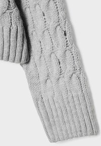 Manche de pull tricoté gris clair avec motif torsadé et détails de poignets côtelés sur fond blanc.