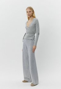 Graues langärmeliges Wickeloberteil mit V-Ausschnitt und Bindedetail, kombiniert mit grauen weit geschnittenen Hose aus weichem Stoff. Das Schuhwerk sind hellbraune Ballerinas.