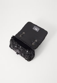 Borsa nera con paillettes, corpo in tessuto morbido, chiusura a patta superiore e dettagli in catena; l'interno foderato rivela un ampio scomparto.