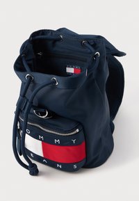 Ναυτικό μπλε σακίδιο με κορδόνι και κόκκινο-άσπρη ρίγα ως διακόσμηση. Διαθέτει μια τσέπη με φερμουάρ στο μπροστινό μέρος και ανθεκτικό υλικό με λεία υφή.