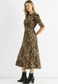 Leopard print midi dress in tan and black, with a fitted bodice, short sleeves, and flowing skirt, paired with black ankle boots.