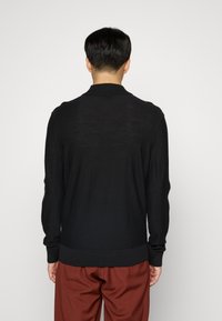 Cardigan noir en tricot avec un col et des poignets côtelés, manches longues et coupe régulière. Finition texturée ajoutant de la profondeur au design.