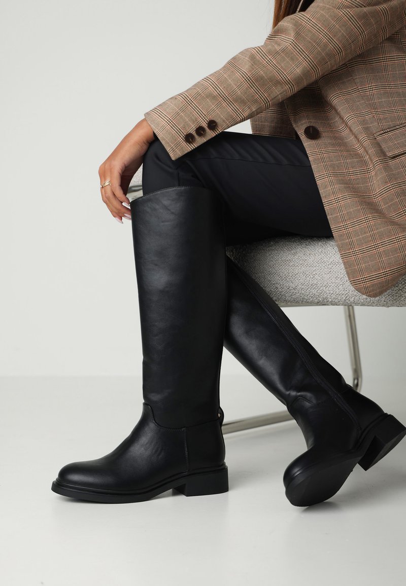 Botas altas de cuero negro con una textura suave, puntera redondeada, tacón bajo tipo bloque y un detalle de cremallera en la parte posterior.