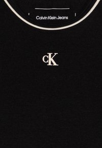 T-shirt noir en coton avec un col rond et un contour blanc contrastant. Présente un petit logo "cK" en blanc au centre.