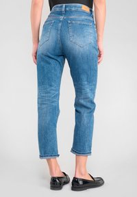 Jean en denim bleu clair avec taille haute, jambes droites et légère décoloration, comportant cinq poches et une étiquette en cuir à l'arrière.