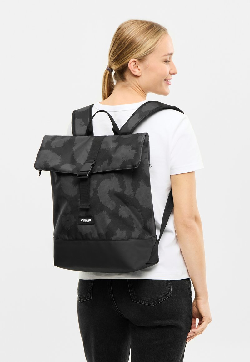 Rucsac negru cu un exterior texturat și cu un model, închidere cu culisare, și curele reglabile; are un panou inferior neted.