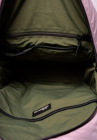Roze rugzak interieur met olijfgroene stof, voorzien van een ritszak en een label. De textuur is glad en licht gekreukt.