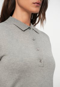 Siva polo majica z klasičnim ovratnikom, šestimi gumbi in mehkobo, teksturirano tkanino. Diskretne šivane podrobnosti ob šivu.