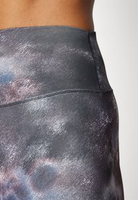 High-waisted leggings in gray with a multicolored abstract pattern. Features smooth fabric with a subtle sheen and flatlock stitching.