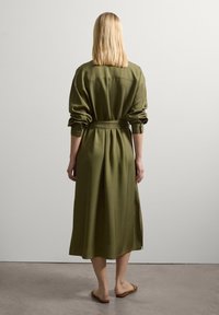 Olivgrünes, langärmeliges Hemdkleid mit einem taillierten Gürtel, geknöpften Bündchen und seitlichen Schlitzen. Glatter Stoff mit einem fließenden Schnitt.