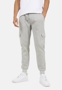 Jasnoszare bawełniane dresy z bocznymi kieszeniami cargo, elastycznym ściągaczem w pasie i ściągaczami przy nogawkach. Dobrane z białymi sneackerami.