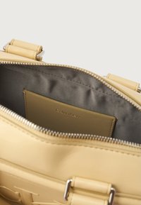 Intérieur d'un sac à main en cuir jaune montrant un doublure en tissu gris et une petite poche pour cartes avec le logo "Calvin Klein" visible. Fermeture à glissière.