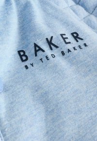Tessuto azzurro chiaro con una superficie liscia, caratterizzato dal testo "BAKER" in lettere nere in grassetto e "by TED BAKER" in un font più piccolo sottostante.