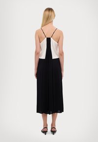 Czarna i biała sukienka bez rękawów z dopasowanym gorsetem i plisowanym tyłem, przechodząca w zwiewną spódnicę. Regulowane ramiączka i miękka tkanina.