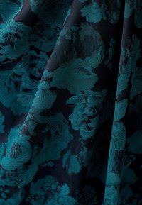 Texturerad tyg med en mörk marin bakgrund och turkosa blommönster, som framhäver intrikata detaljer och en rik färgkontrast.