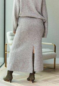 Lysegrå strikket sweater og matchende nederdel med en sideslids, parret med olivengrønne højhælede støvler. Blød tekstur, afslappet pasform.