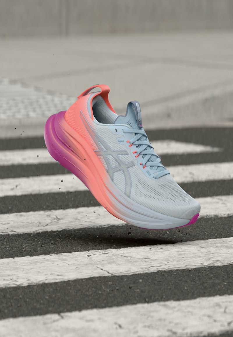 Light blue and pink running shoe mid-air above a pedestrian crossing on an asphalt road.