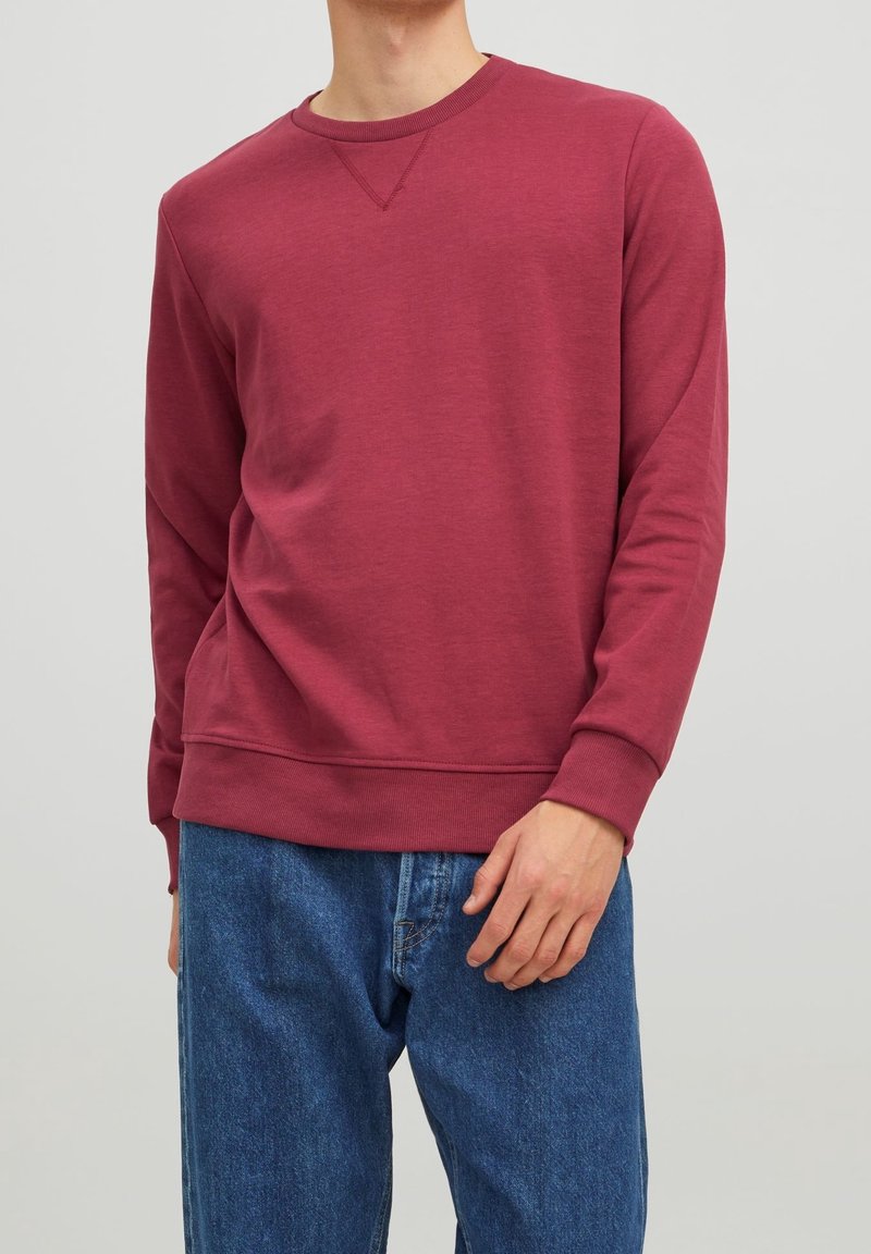 Felpa bordeaux a girocollo con maniche lunghe, caratterizzata da una finitura texturizzata e polsini a costine, abbinata a jeans in denim blu.