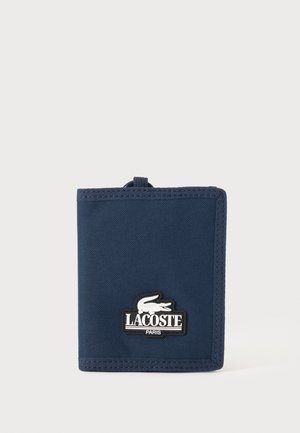 Granatowy materiałowy portfel z naszywką z logo Lacoste Paris przedstawiającym białego krokodyla, pokazany zamknięty na białym tle.